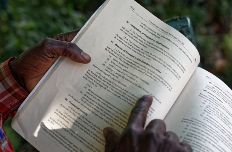 Hands holding an open copy of the Zimbabwe Constitution